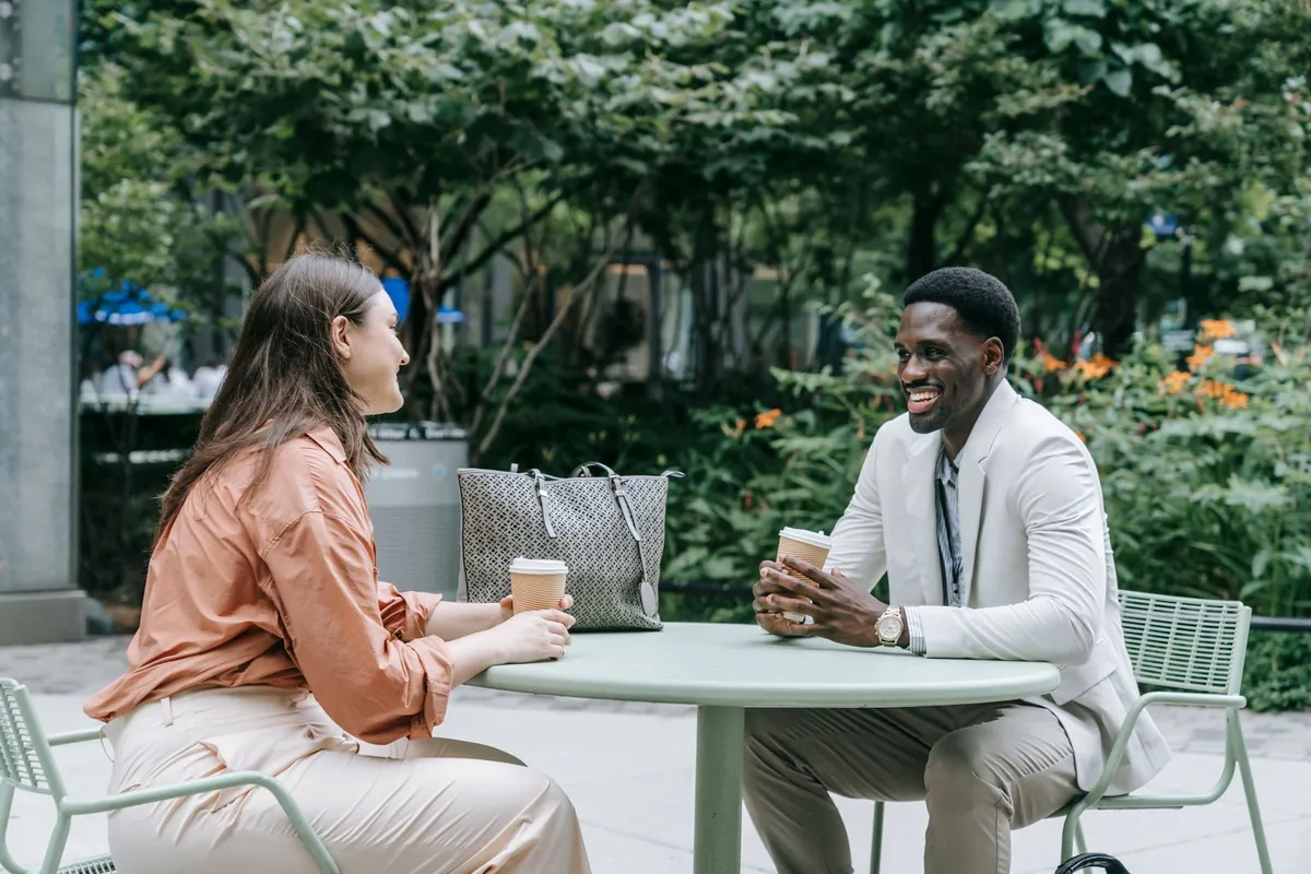 Two people at an outdoor café table with coffee, talking