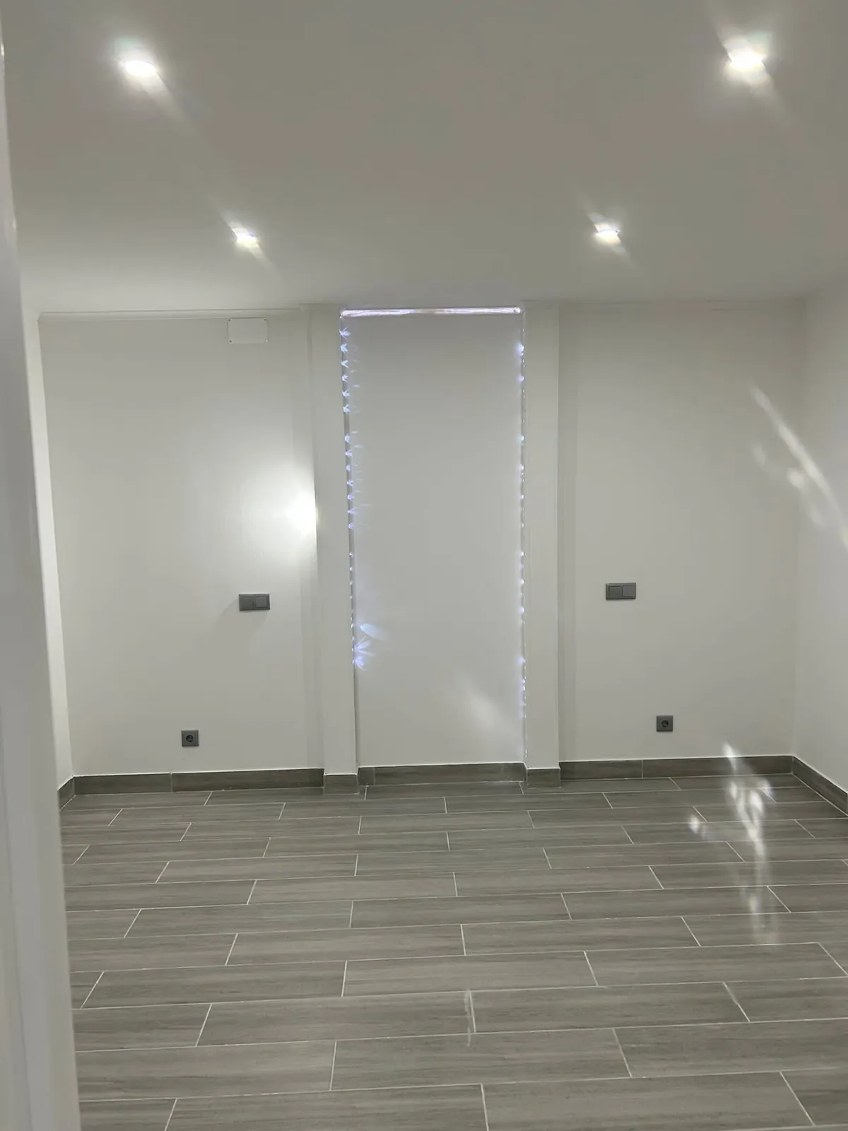 Sala remodelada com focos de luz no teto, tomadas e chão de madeira