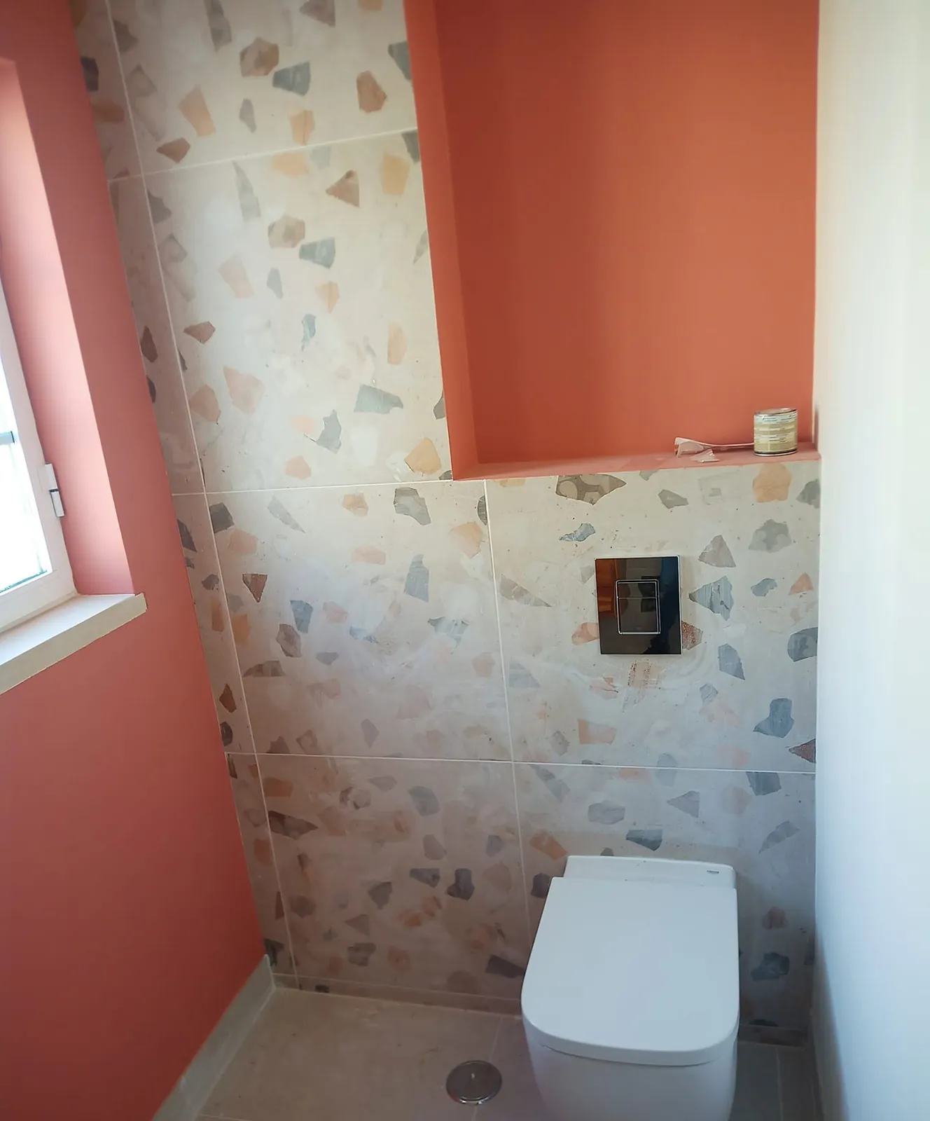 Casa de banho com sanita, placa do autoclismo embutido e nicho cor de coral