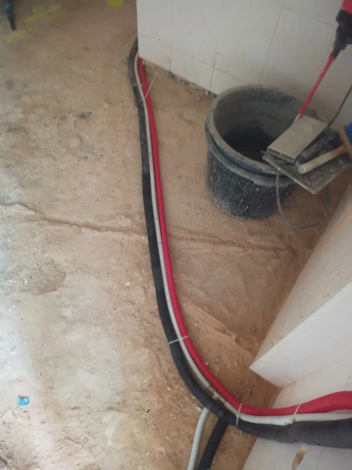 Chão em obra com tubos vermelhos e pretos encostados à parede