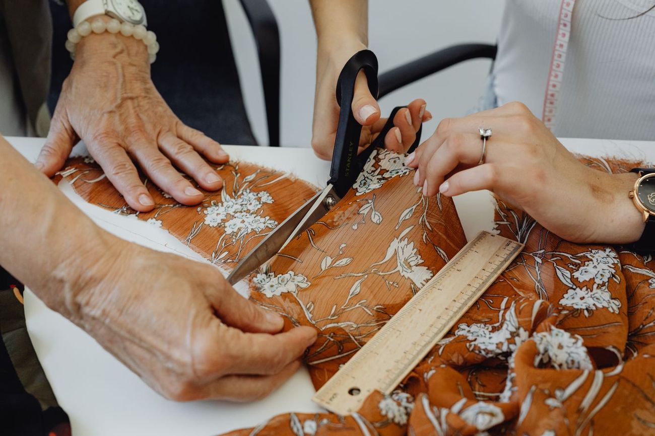 Mãos a cortar tecido estampado com régua e tesoura