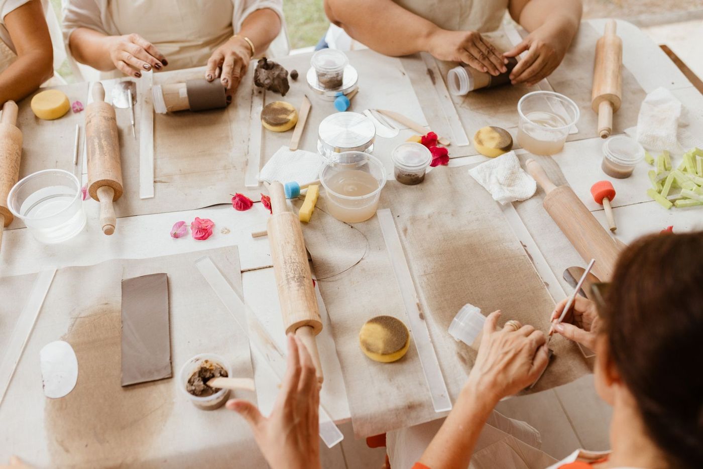 Uma mesa de workshop vista de cima, com várias mãos a trabalhar o barro