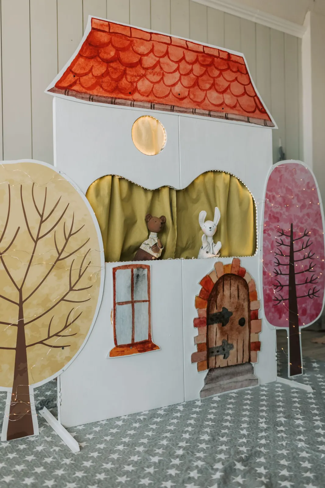 Teatro de fantoches em forma de casa, com telhado vermelho e árvores pintadas