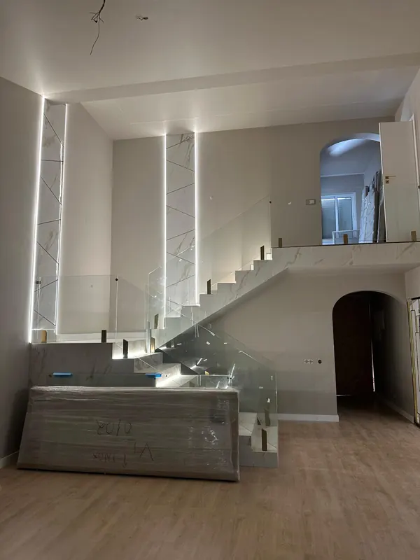 Escada revestida a mármore branco com guarda em vidro e iluminação LED, numa sala de pé-direito duplo remodelada