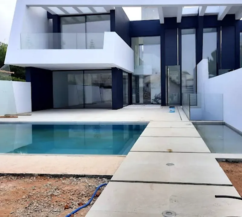 Moradia contemporânea com piscina, grandes envidraçados e passadiço em pedra, com o exterior ainda em obra
