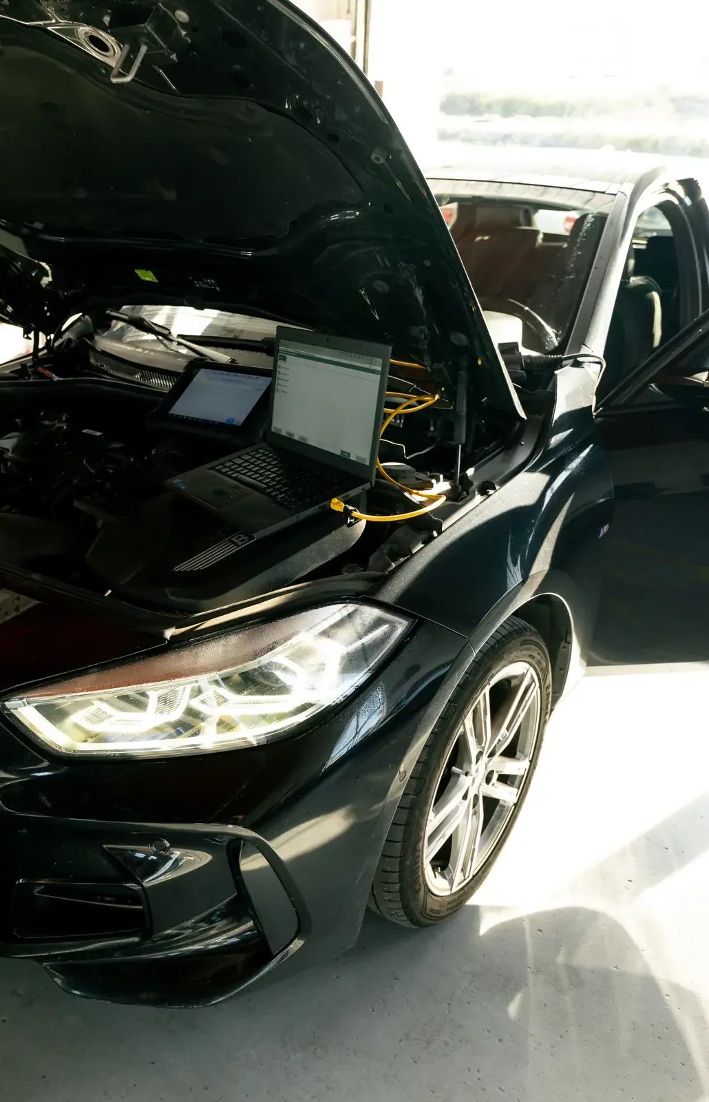 Computador de diagnóstico ligado a um BMW preto de capô aberto
