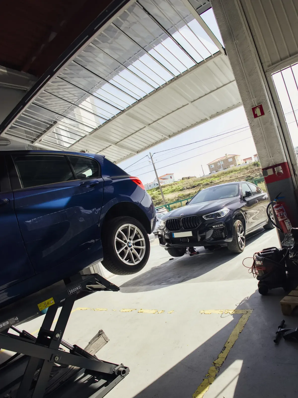 BMW azul no elevador e BMW X6 à entrada da oficina