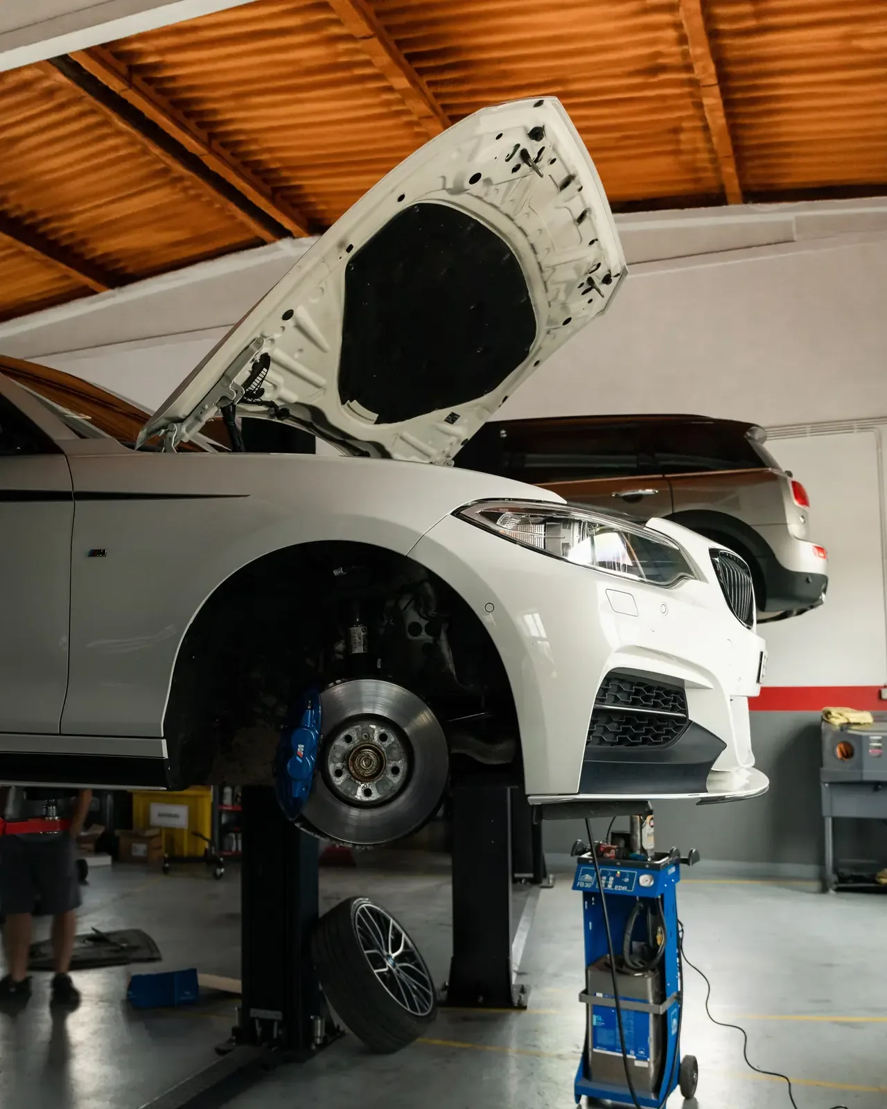 BMW branco no elevador, sem a roda, com o disco e a pinça de travão à vista